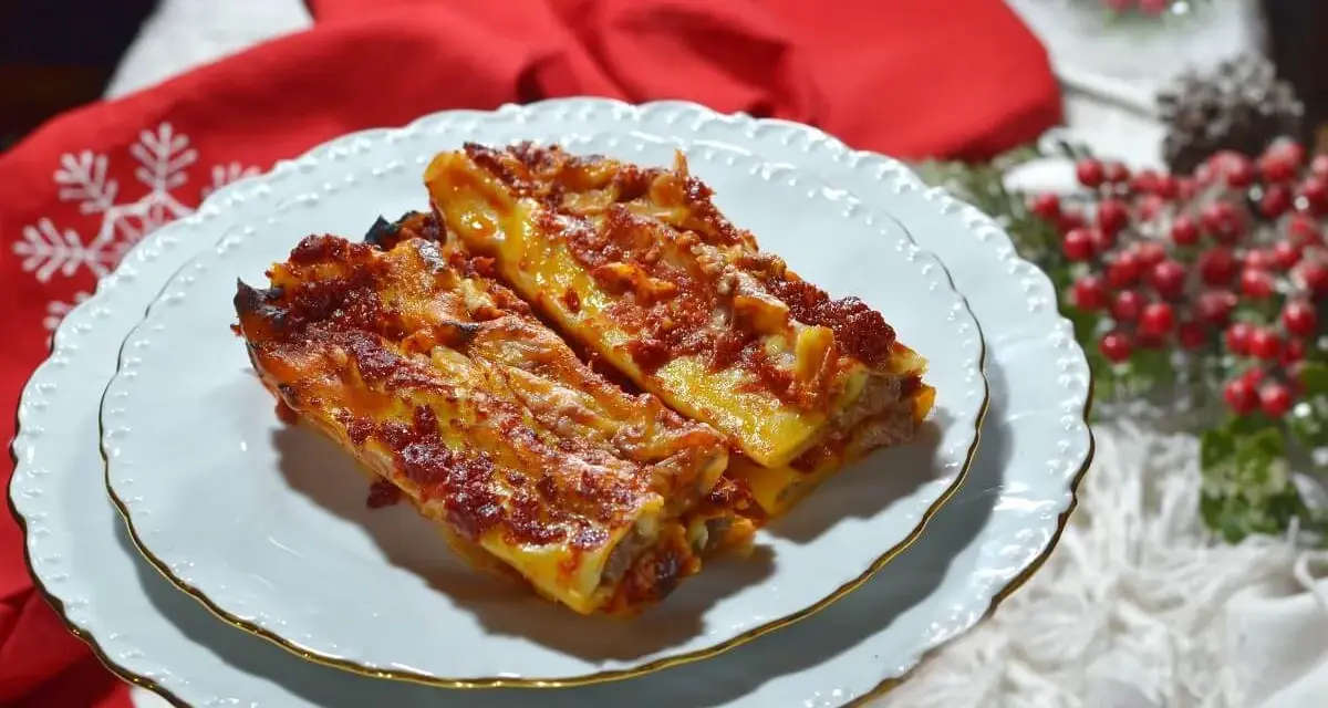 Due cannelloni di carne fumanti, ricoperti di sugo rosso e formaggio filante, serviti su un piatto bianco con bordo dorato, pronti per essere gustati.