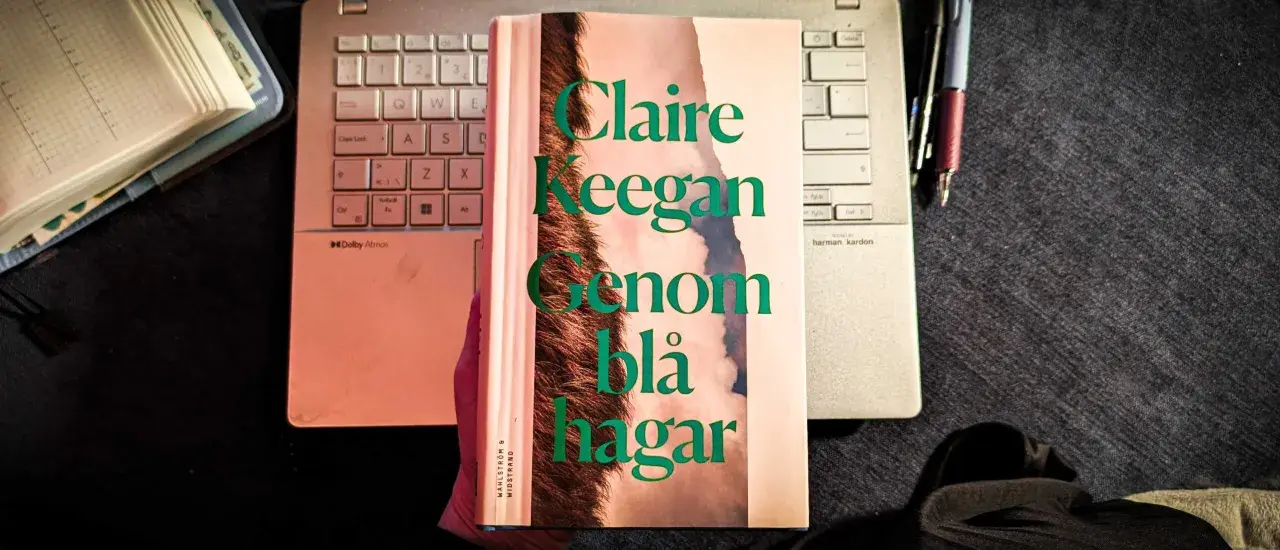 Claire Keegans bok "Genom blå hagar" ligger på ett tangentbord bredvid en anteckningsbok och pennor.