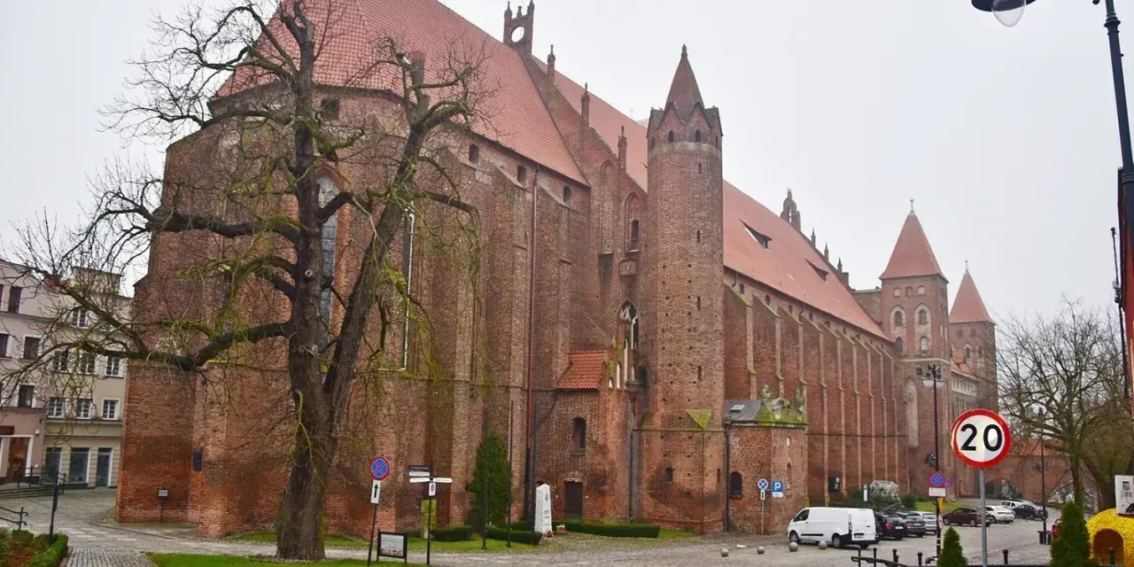 Imponująca katedra w Kwidzynie, z cegły, z charakterystycznymi wieżami i czerwonym dachem, otoczona drzewami i budynkami.