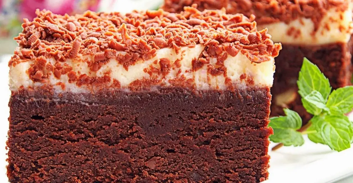 Pyszny torcik brownie z kremową warstwą i posypką czekoladową, ozdobiony listkami mięty.