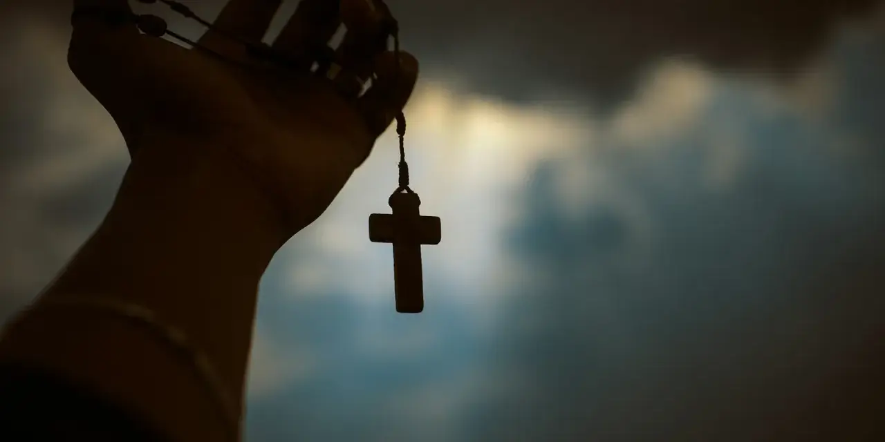 Dłoń trzyma paciorki różańca z krzyżem, symbolizując poszukiwanie prawdy w obliczu niepewności, jak agnostycyzm.