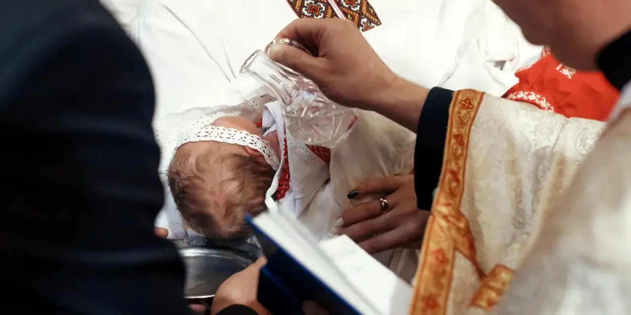 Ceremonia chrztu dziecka. Duchowny polewa główkę niemowlęcia wodą święconą. Warto wiedzieć, ile kosztuje chrzest.