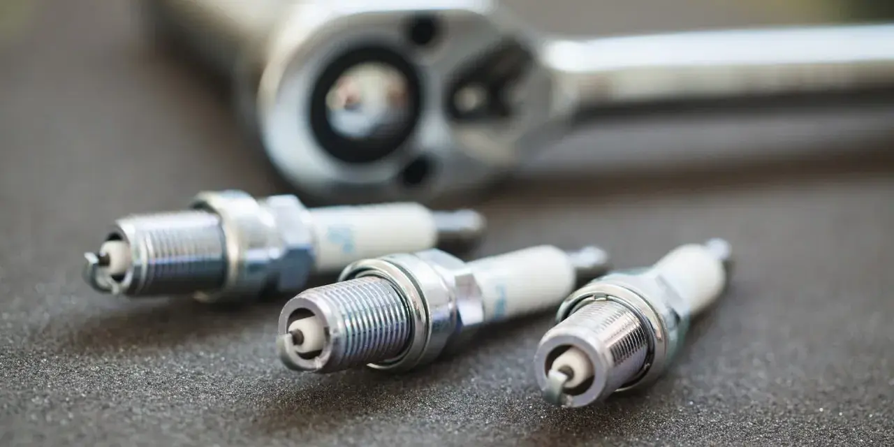 Three spark plugs and a ratchet are laid out, ready for a tune-up. The image highlights the importance of knowing the correct spark plug socket size for the job.
