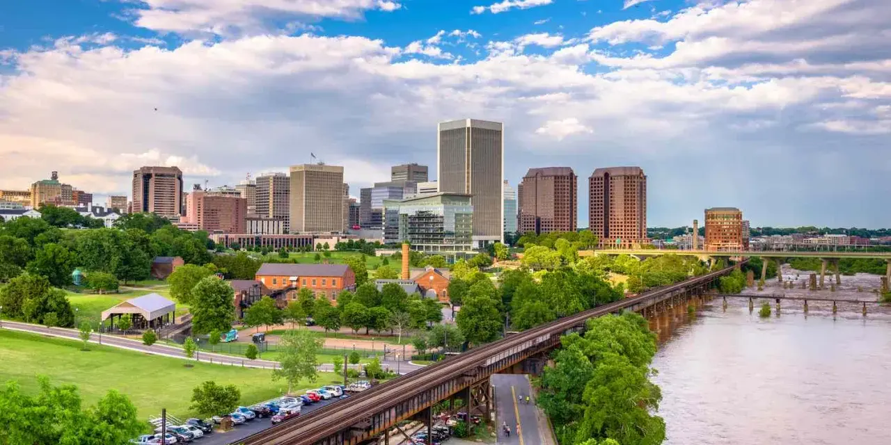 A scenic view of Richmond, VA, showcasing the city skyline, a river, and a railway bridge. Perfect for a weekend getaway.