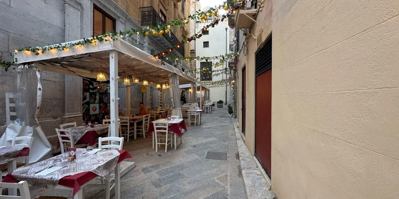 Urocza uliczka w Trapani, gdzie zjeść? Stoliki restauracyjne pod girlandami z cytryn i lampek, idealne na wieczorny posiłek.