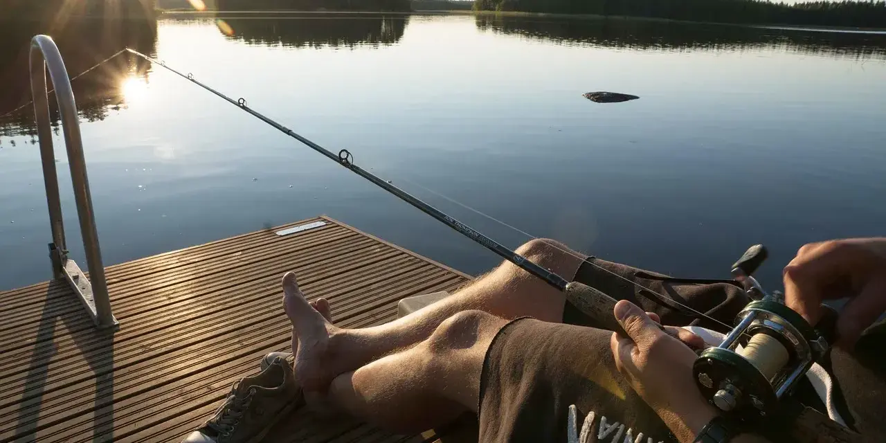Spokojny dzień nad jeziorem Urszulewskim. Wędkarz czeka na branie, słońce zachodzi, odbijając się w spokojnej tafli wody.