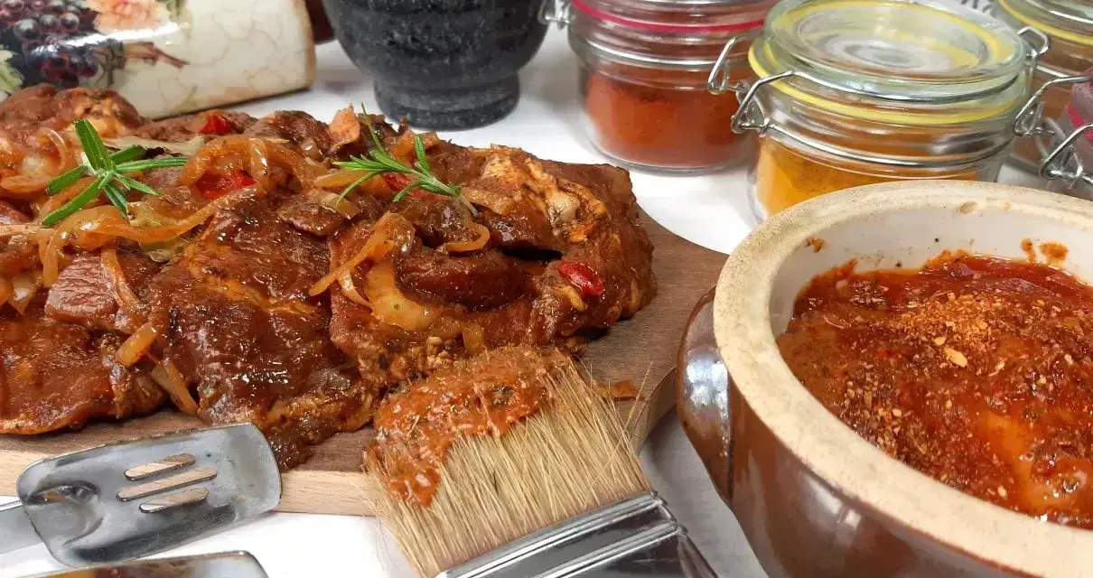 Karkówka na grilla w aromatycznej marynacie, gotowa do pieczenia. Obok pędzel z marynatą i słoiczki z przyprawami.