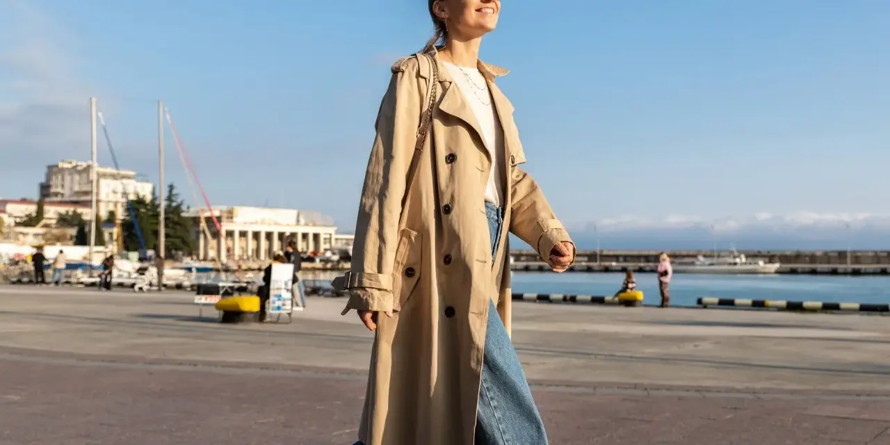 Una chica con estilo, con un look clean girl, pasea por el puerto con un abrigo beige y vaqueros anchos.