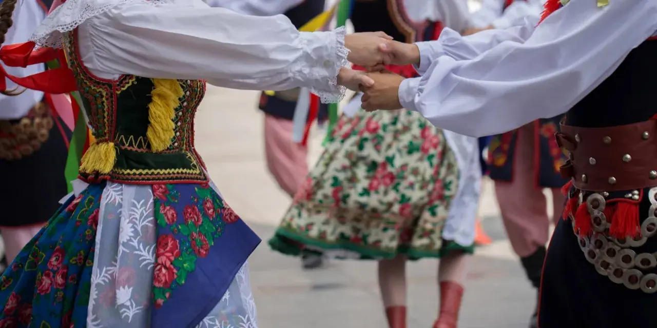 Tancerze w barwnych strojach ludowych, żywa muzyka folkowa w tle.