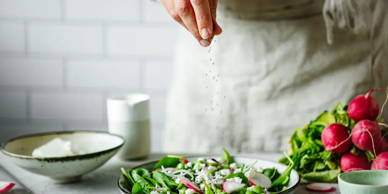 Une main saupoudre des graines sur une salade fraîche. Une idée pour une recette de radis noir.