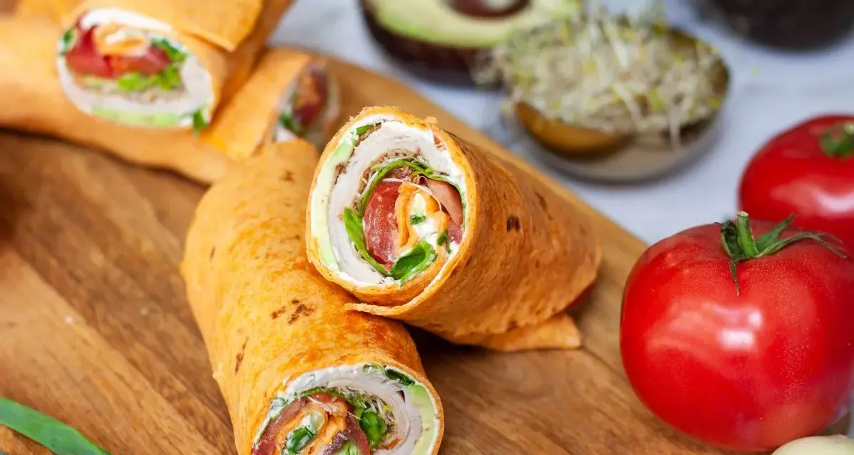 Pyszna tortilla na śniadanie z warzywami i kremowym serkiem. Obok pomidory, awokado i kiełki.