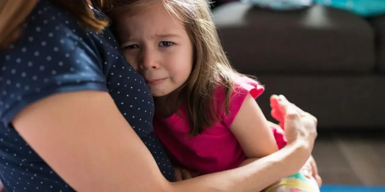 Mała dziewczynka płacze, wtulona w mamę. To właśnie parenting – trudne chwile i bezwarunkowa miłość.