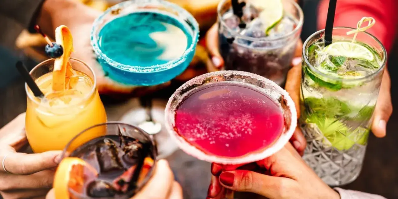 Kolorowe, popularne drinki w rękach przyjaciół. Różowe, niebieskie, pomarańczowe i zielone koktajle z owocami i lodem.
