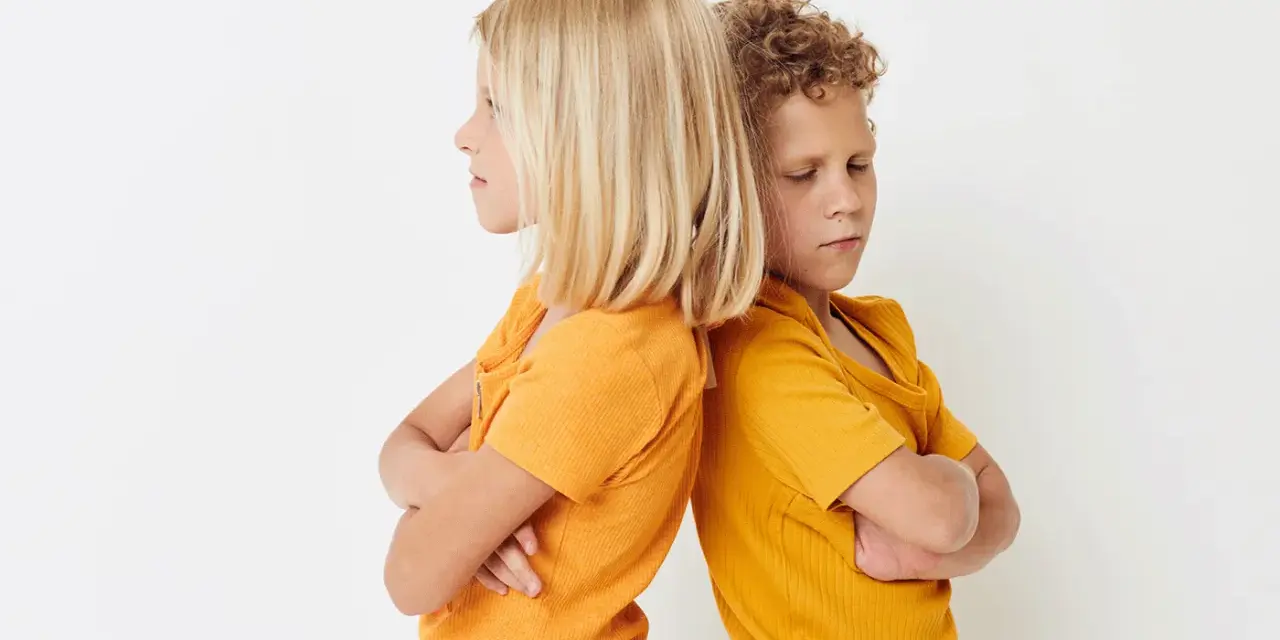 Zwei Kinder stehen mit verschränkten Armen Rücken an Rücken. Ihre Mimik deutet auf **Gewalt unter Geschwistern** hin, ein Streit, der sie trennt.