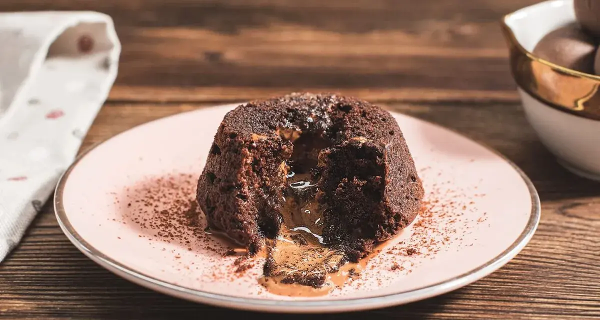 Coulant de chocolate con centro líquido y cremoso, espolvoreado con cacao en polvo sobre un plato rosa.