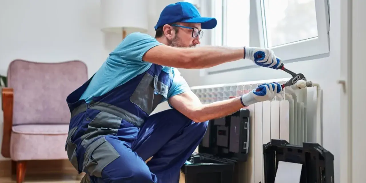 Tecnico con attrezzi effettua manutenzione termosifoni vicino a una finestra.