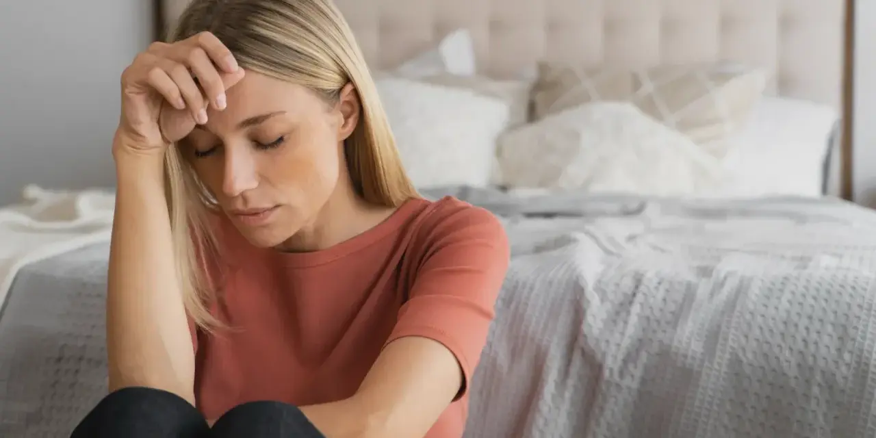 Kvinna med slutna ögon, handen mot pannan. Kanske en känsla av depression under klimakteriet, men det finns behandling.