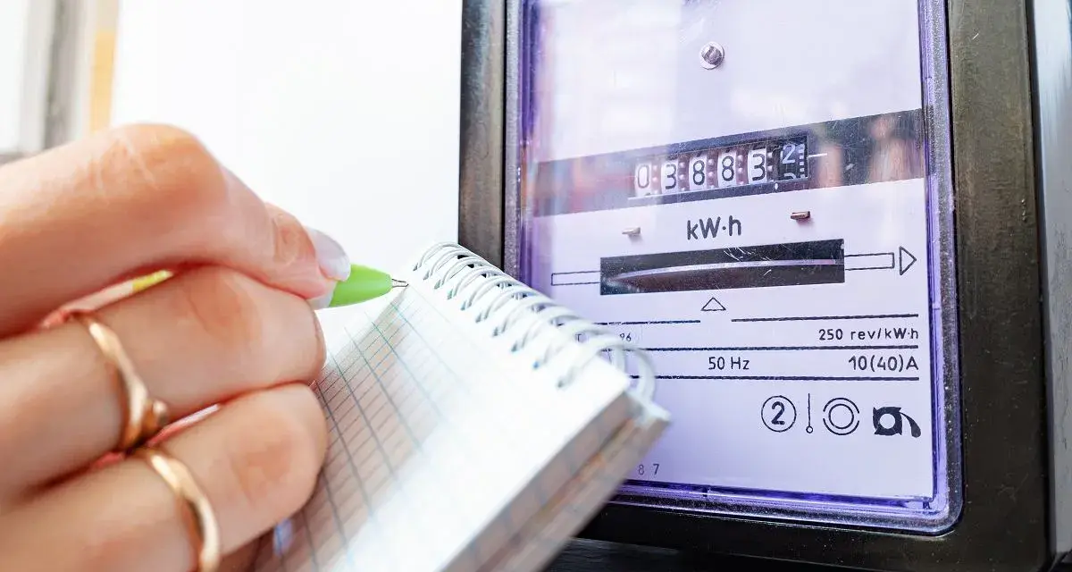 Dłoń z pierścionkami zapisuje odczyt licznika energii elektrycznej, by sprawdzić rachunek za prąd.