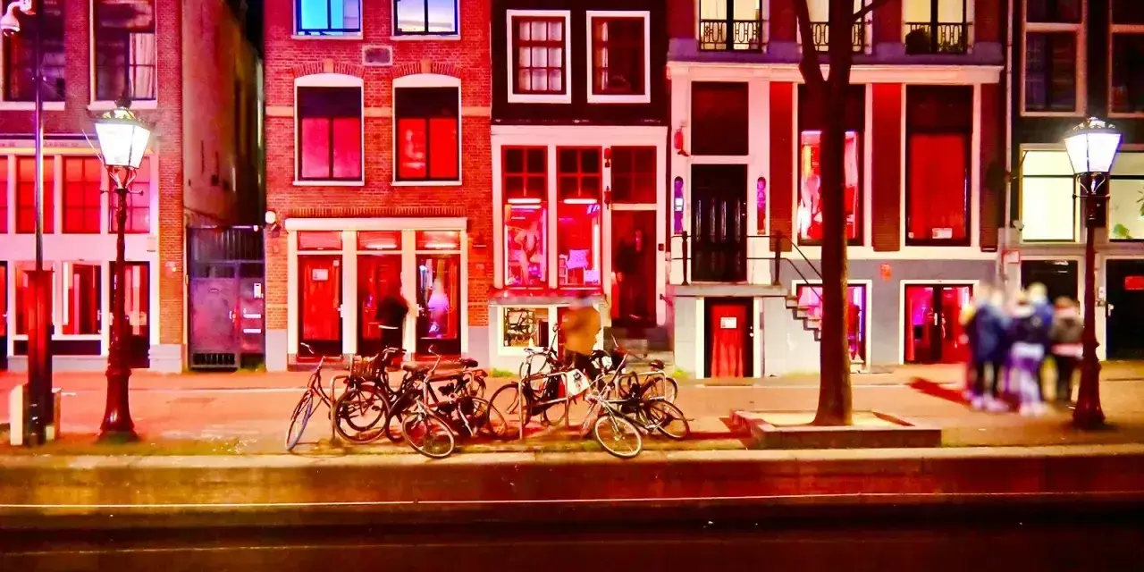 Nocna czerwona ulica Amsterdamu, z oświetlonymi oknami i kanałem odbijającym światła.