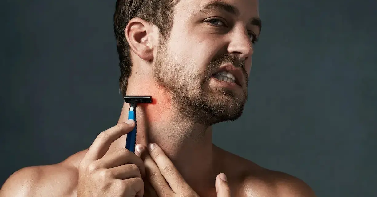 Hombre con piel irritada afeitado, se rasca el cuello con una navaja de afeitar azul.