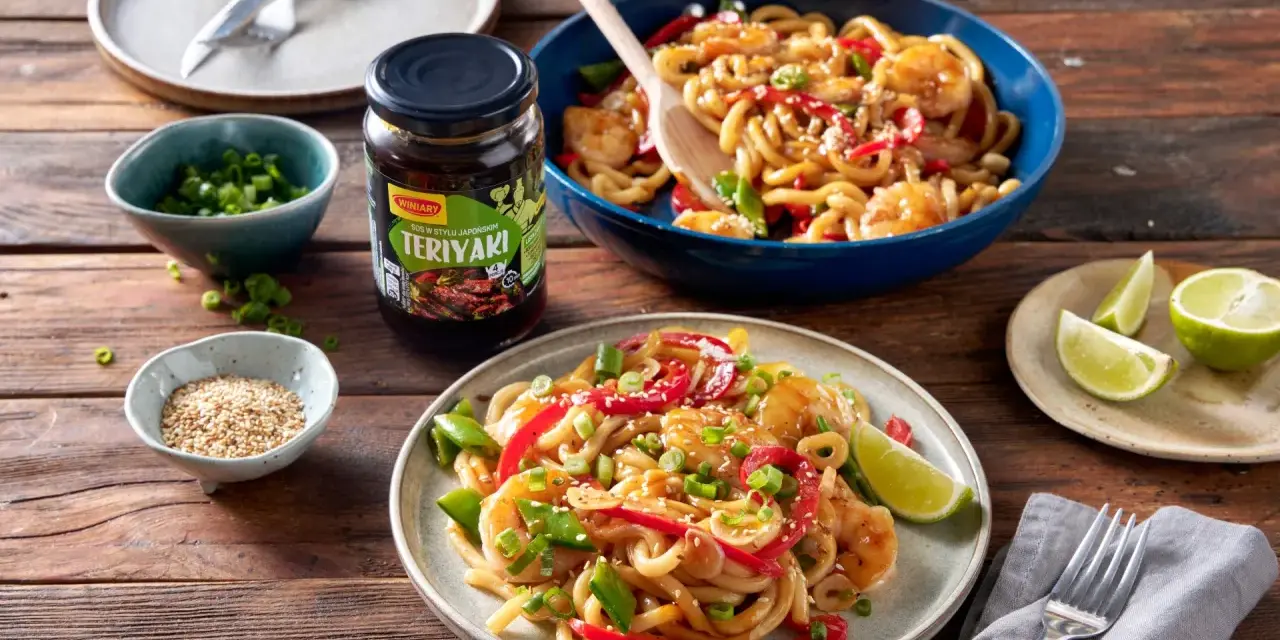 Krewetki z makaronem w sosie teriyaki, podane na talerzu z dodatkami.