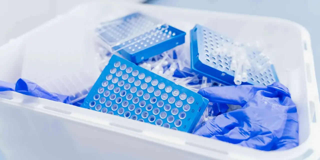 Niebieskie płytki do pipetowania i rękawiczki w pojemniku na odpady laboratoryjne. Kod odpadu 16 03 04.