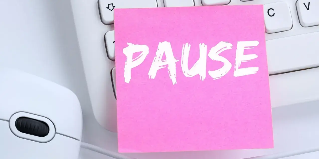 Ein rosa Zettel mit dem Wort "PAUSE" liegt auf einer Tastatur neben einer Maus. Ein Hinweis auf das **bildschirmpause gesetz**.