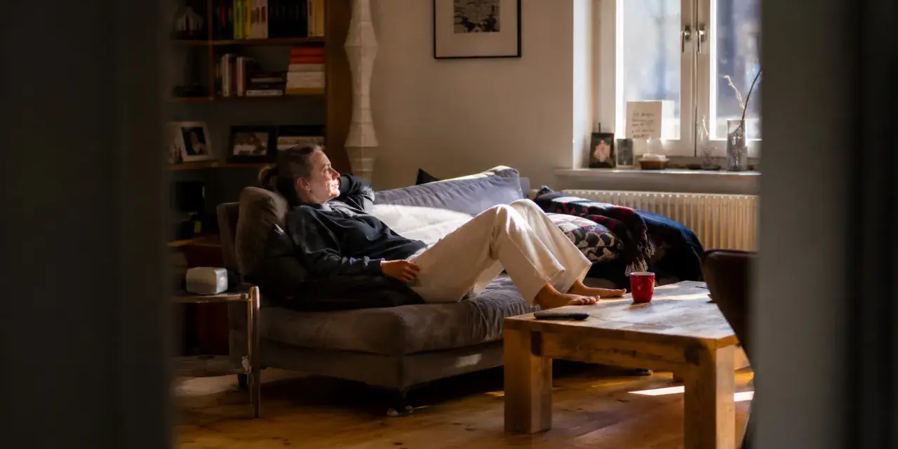 Frau liegt auf Sofa, genießt stille Meditation im warmen Sonnenlicht. Ein Moment der Ruhe im gemütlichen Wohnzimmer.