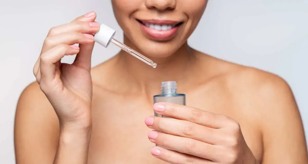 Une femme souriante applique un sérum. Elle se demande combien de temps entre sérum et crème pour une peau parfaite.