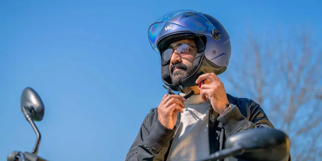 Uomo con barba che indossa un casco da moto blu iridescente, pronto per un giro.