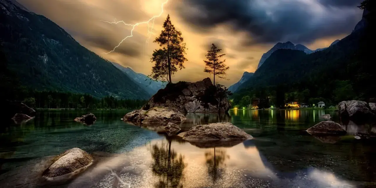 Dramatyczne zdjecia hdr: błyskawica nad skalistą wyspą z drzewami na środku jeziora, otoczonego górami.