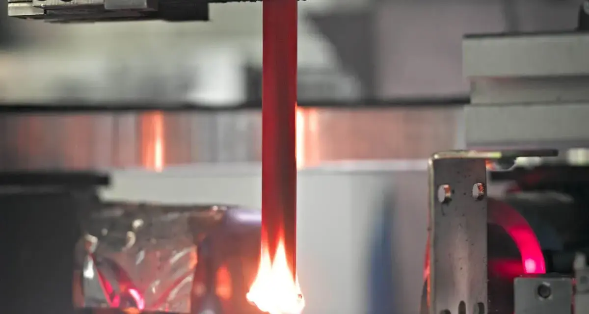 A red acrylic rod is tested for how acrylic fire resistant it is, with a flame licking its base.