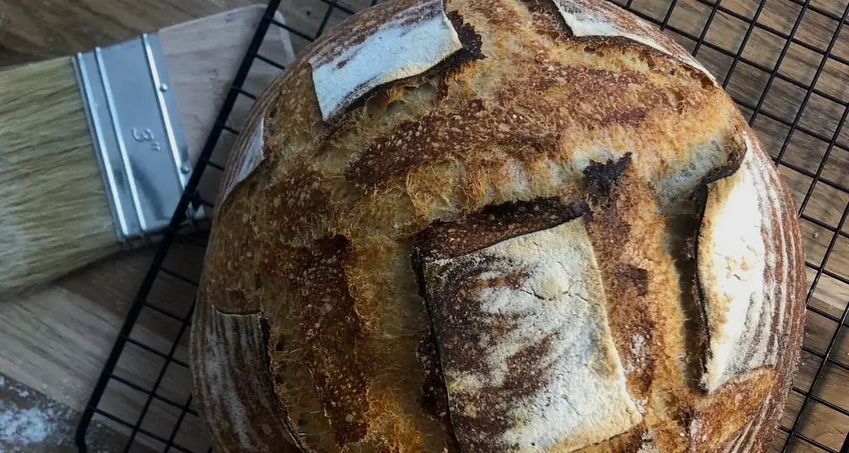 Chleb pszenno żytni na zakwasie, pachnący świeżością, czeka na ostygnięcie. Obok pędzel do pieczenia.
