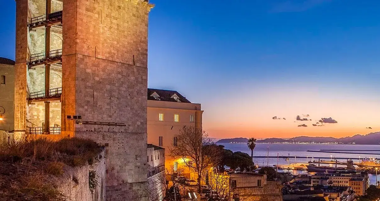 Torre medievale illuminata al tramonto, con vista sul porto e sul mare. Un'ottima anteprima di cosa vedere a Cagliari in un giorno.