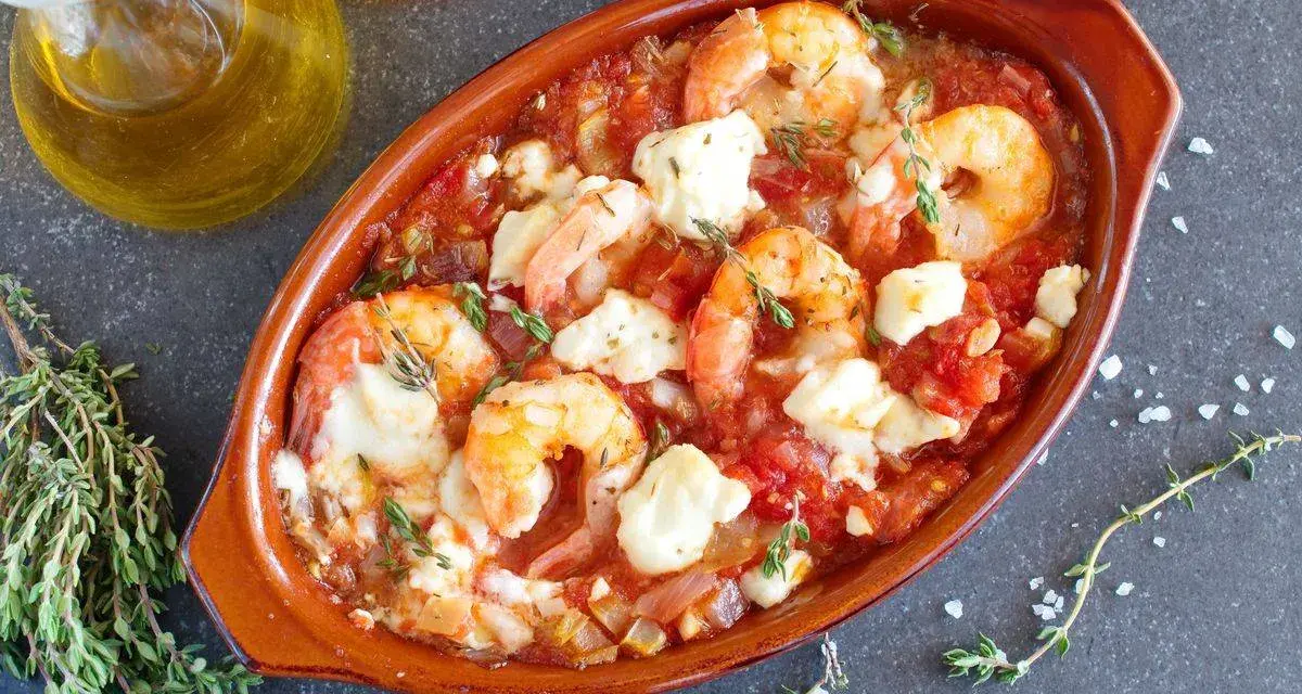 Gamberoni al guazzetto in terracotta, con pomodoro, formaggio fuso e timo. Un piatto invitante pronto per essere gustato.