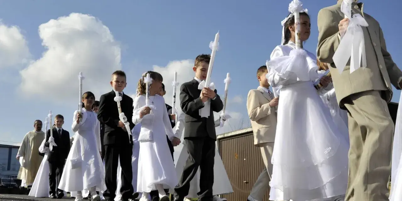 Kinder in festlicher Kleidung, was zieht man zur Kommunion an? Mädchen in weißen Kleidern, Jungen in Anzügen, alle tragen Kerzen.