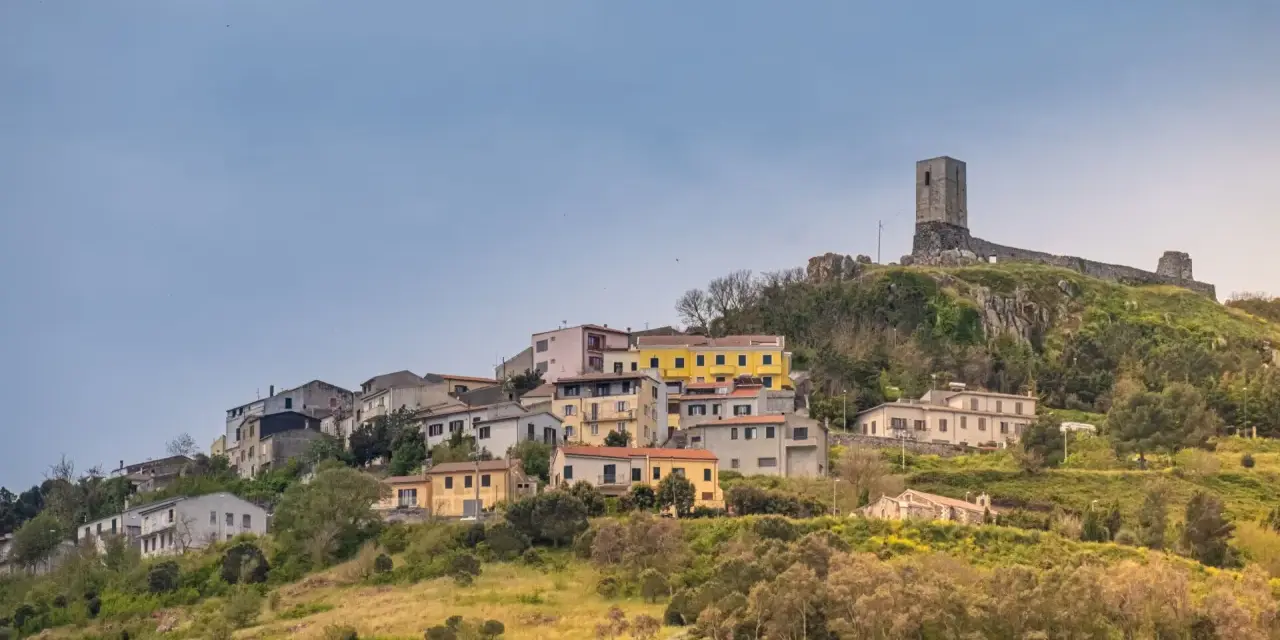 Il castello di Osilo domina un borgo colorato su una collina verdeggiante, sotto un cielo azzurro.