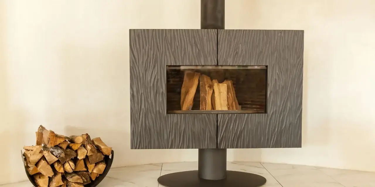Un poêle moderne avec une cheminée vitrée et du bois de chauffage dans un panier. La **déco derrière un poêle** est sobre, mettant en valeur l'âtre.