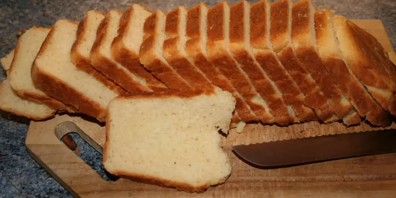 Tranches de pâte à pain de mie dorées et moelleuses, prêtes à être dégustées sur une planche en bois avec un couteau.
