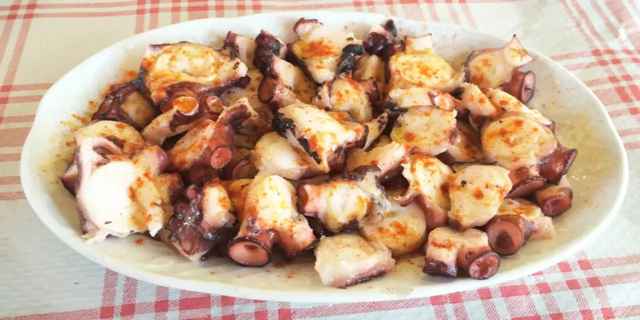 Pulpo a la gallega servido en plato blanco sobre mantel a cuadros rojos y blancos.