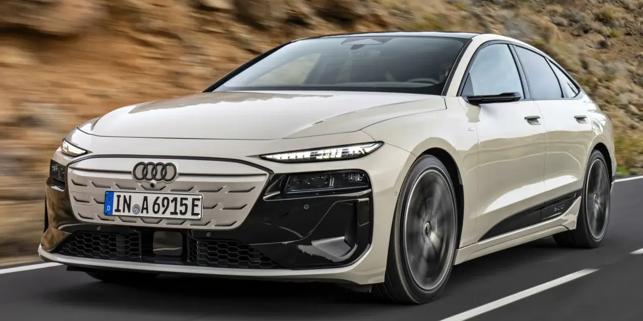 Jasnoszary Audi A6 e-tron z czarnymi akcentami jedzie po drodze.