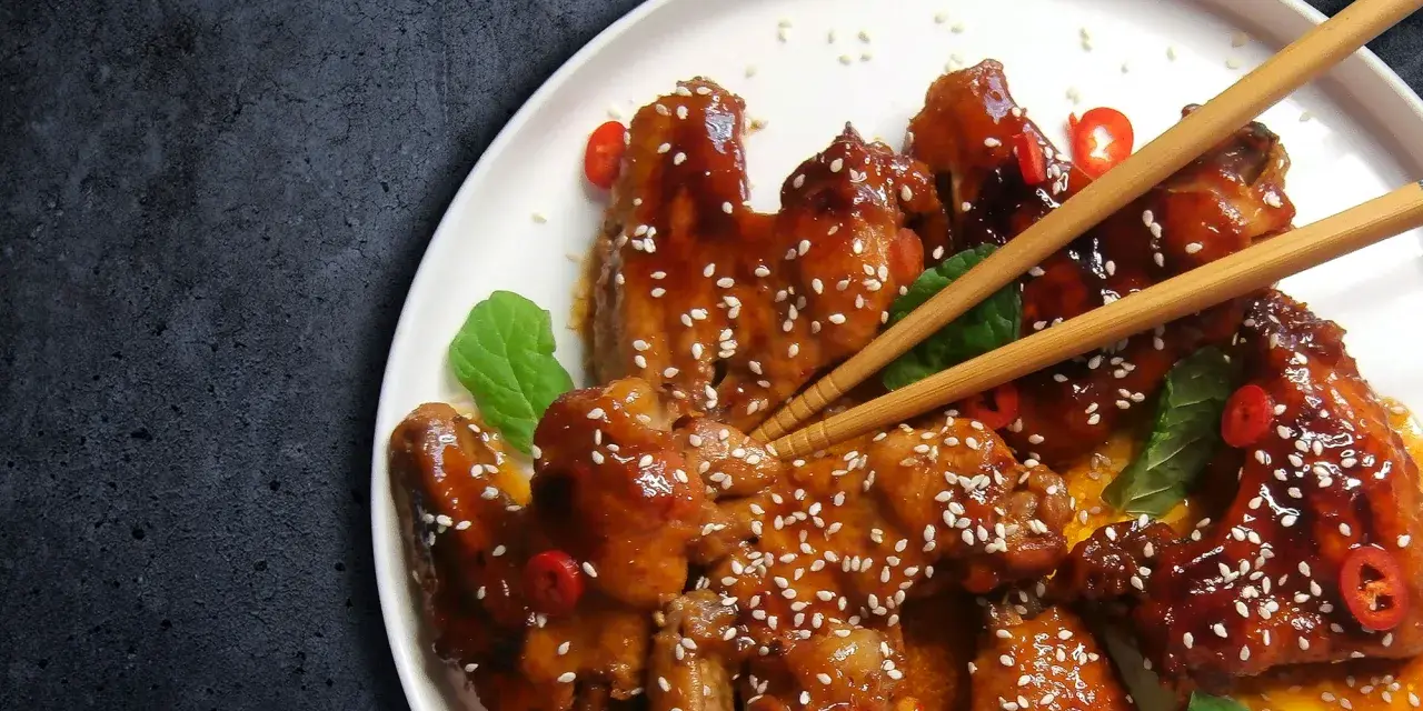 Pyszne skrzydełka teriyaki, błyszczące od sosu, posypane sezamem i ozdobione plasterkami chili.
