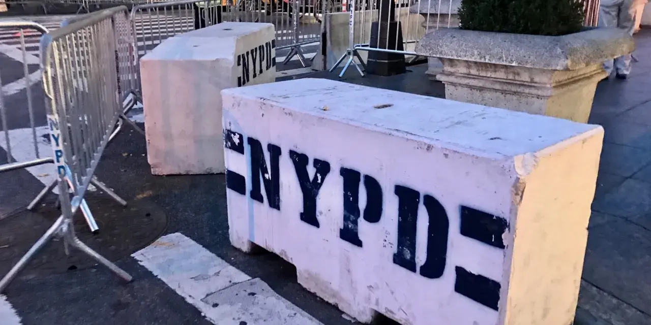 Betonowe bariery NYPD na ulicy. Czy w USA jest bezpiecznie? Widać ludzi i ruch uliczny w tle.