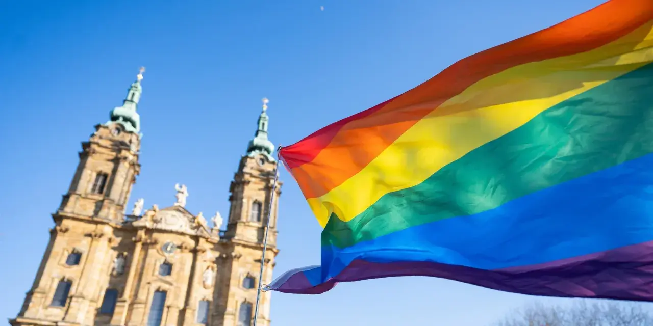 Regenbogenfahne weht vor evangelischer Kirche. Ein Zeichen für Akzeptanz und Vielfalt, das die Botschaft der evangelischen Kirche LGBT widerspiegelt.