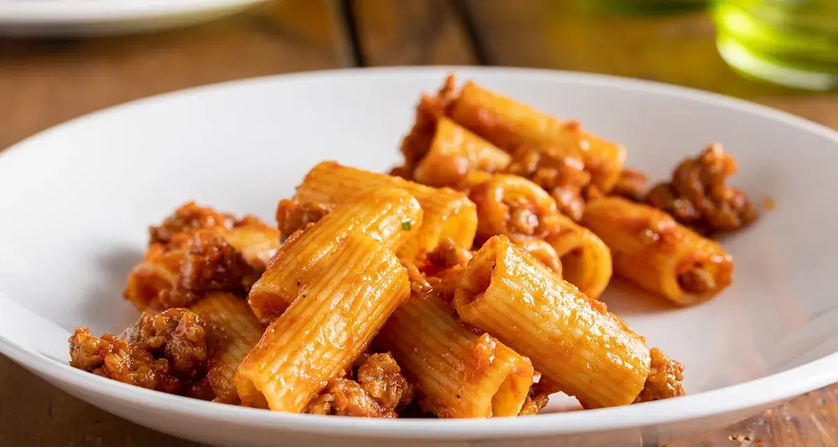 Rigatoni conditi con un ricco ragù di salsiccia, serviti su un piatto bianco.