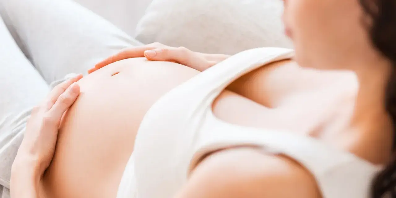 Kobieta w 7 miesiącu ciąży delikatnie głaszcze swój brzuszek.
