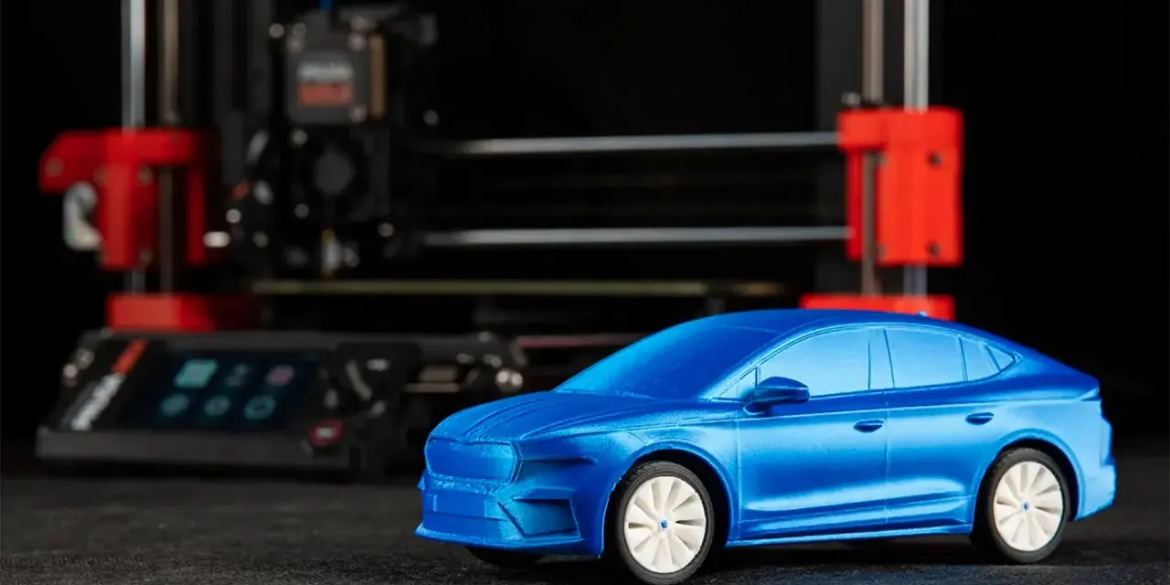 Niebieski model samochodu, gotowy do drukowania, stoi przed drukarką 3D.