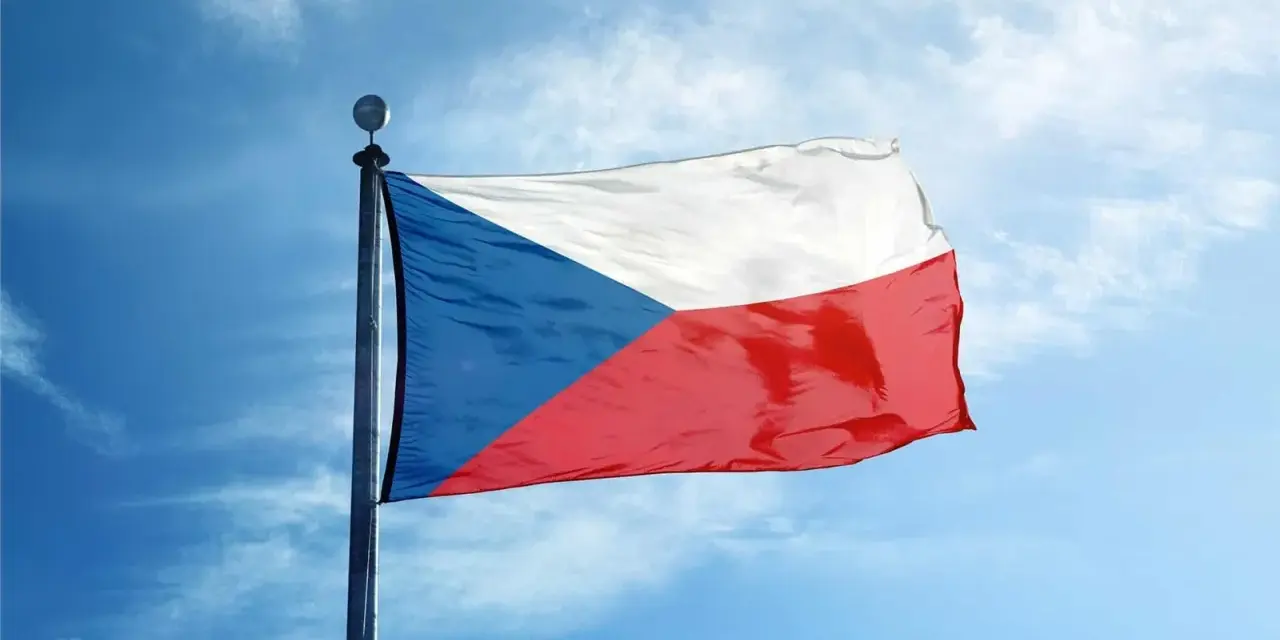 Flaga Czech powiewa na maszcie na tle błękitnego nieba z chmurami.