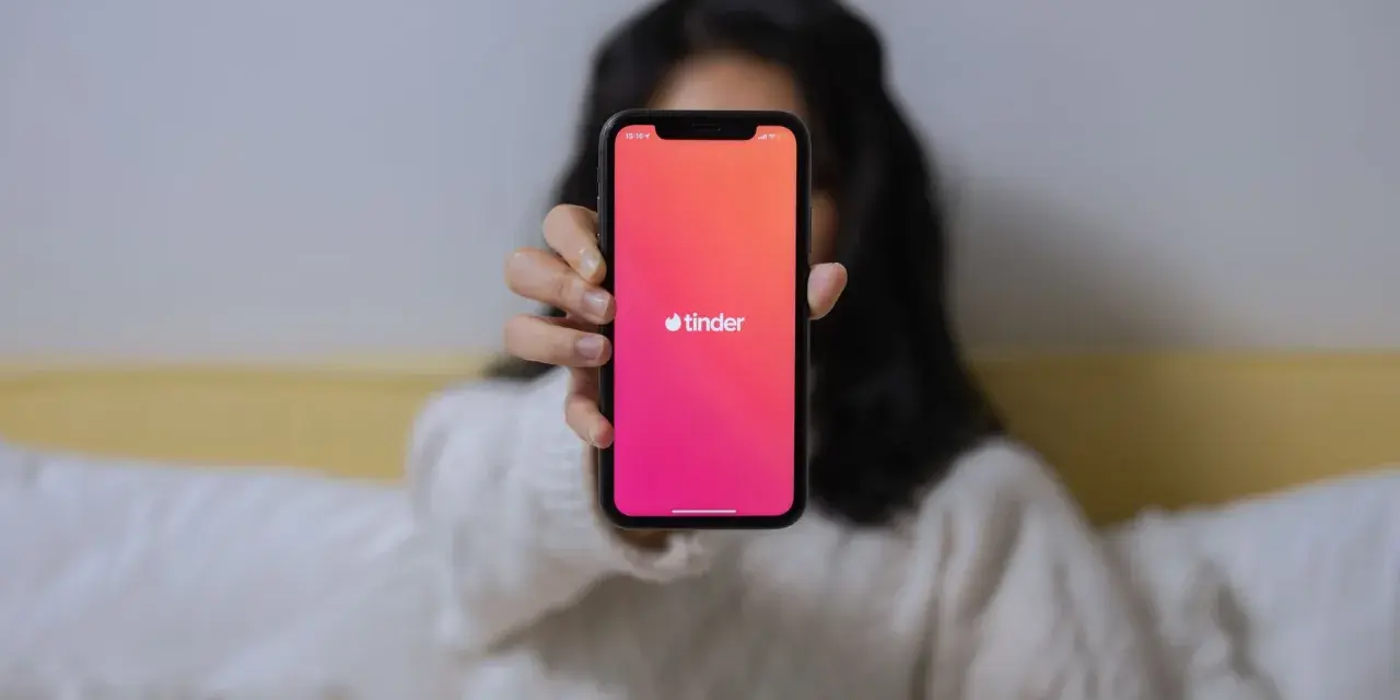 Osoba trzyma telefon z widocznym logo Tindera. Chcesz wiedzieć, jak sprawdzić, czy ktoś ma Tindera?