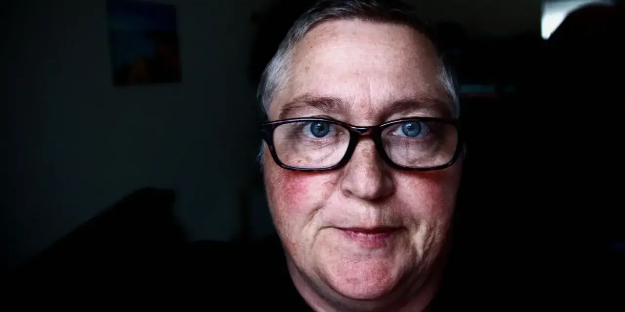 Mężczyzna z niebieskimi oczami i okularami. Jego **czerwona twarz** emanuje ciepłem, a na policzkach widać rumieńce.